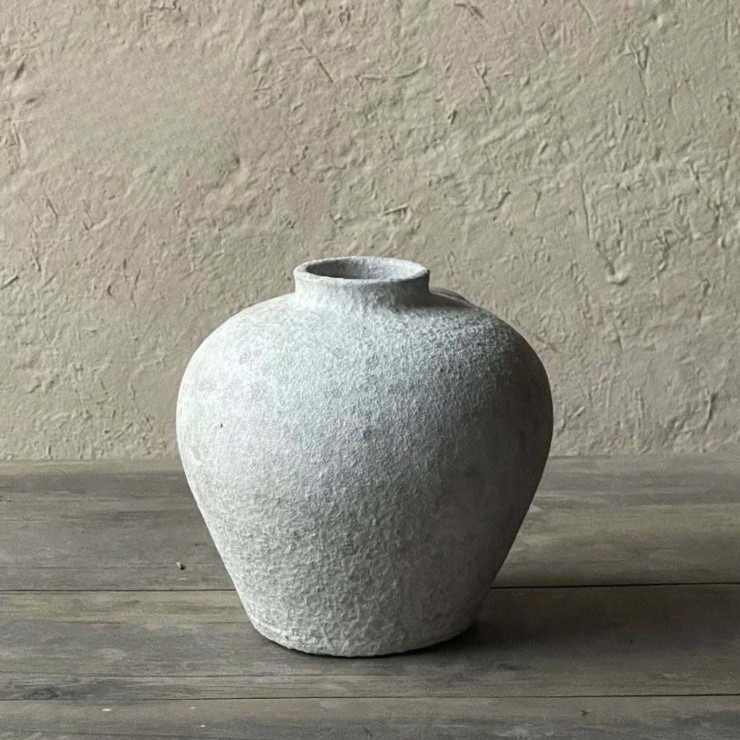 Round textured ceramic vase with narrow neck on rustic wooden table, neutral background