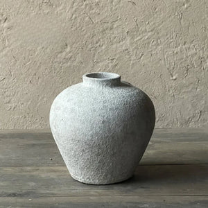 Round textured ceramic vase with narrow neck on rustic wooden table, neutral background