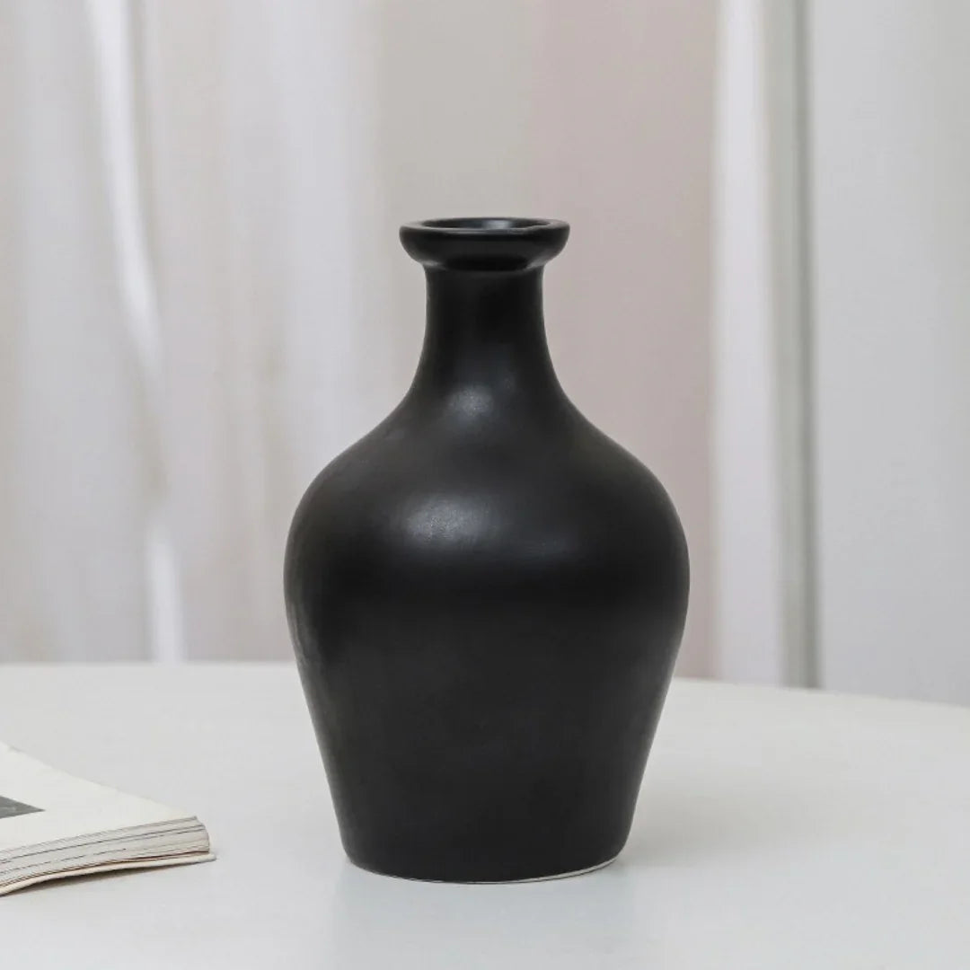Matte black ceramic vase with wide body and narrow neck on white table