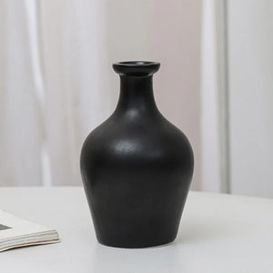Matte black ceramic vase with wide body and narrow neck on white table