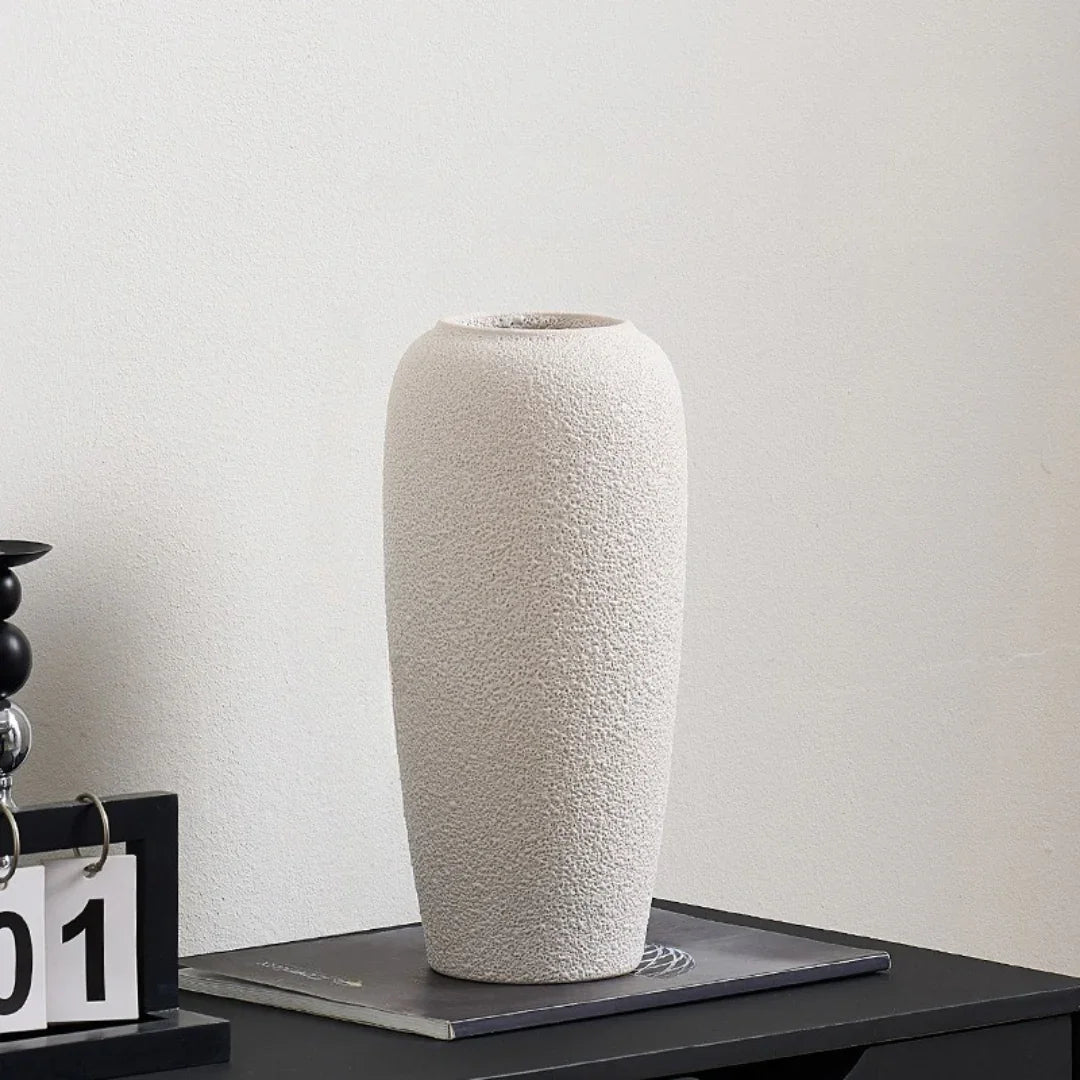 Tall textured ceramic vase in light beige on modern black table against white wall