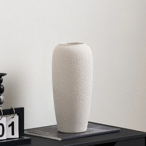 Tall textured ceramic vase in light beige on modern black table against white wall