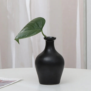 Minimalist black ceramic vase with green leaf on white table, modern home decor