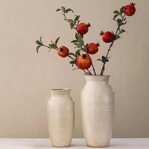 Two beige ceramic vases with branches of red pomegranate fruit and green leaves inside.
