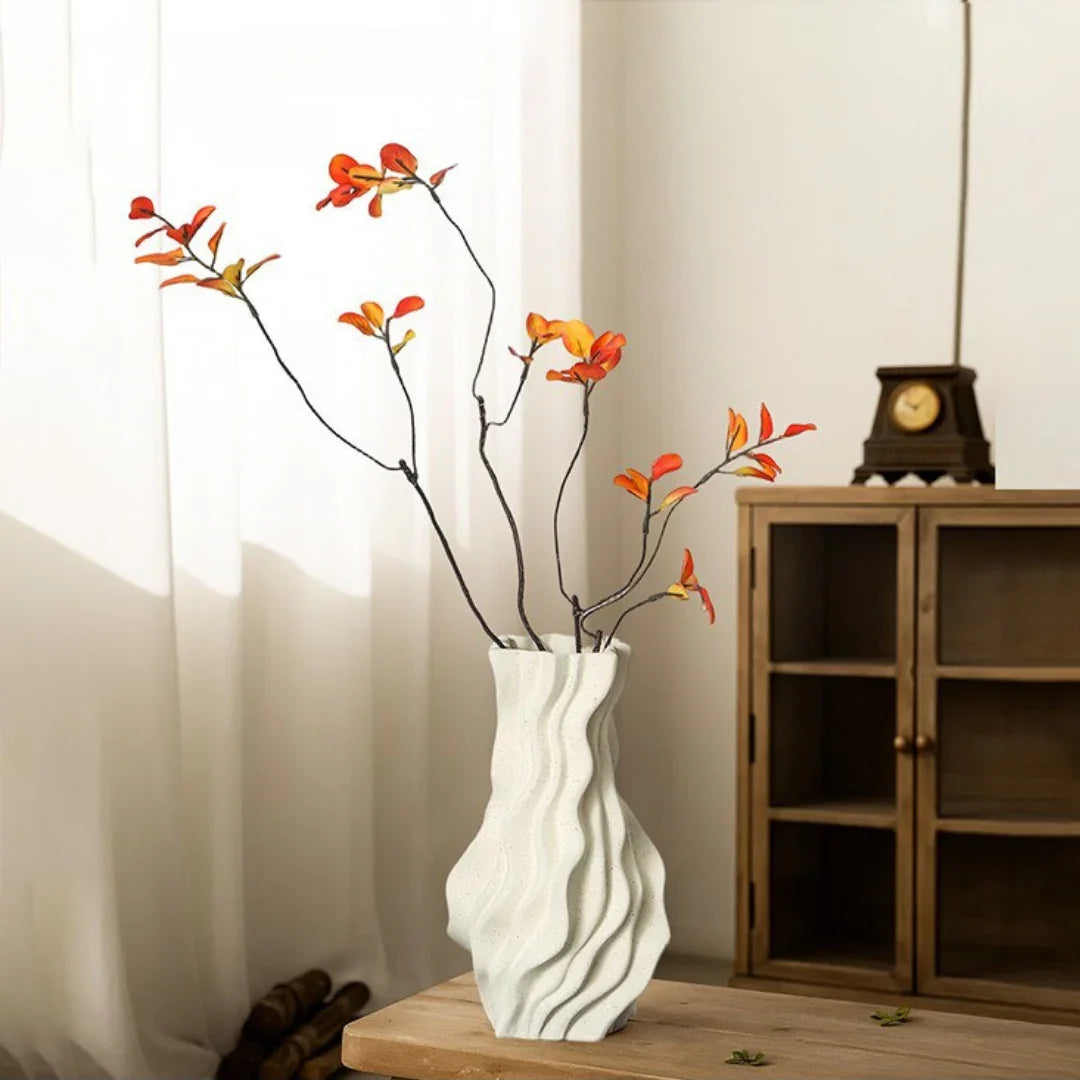Modern wavy white vase with orange artificial flowers on wooden table in a cozy living room setting