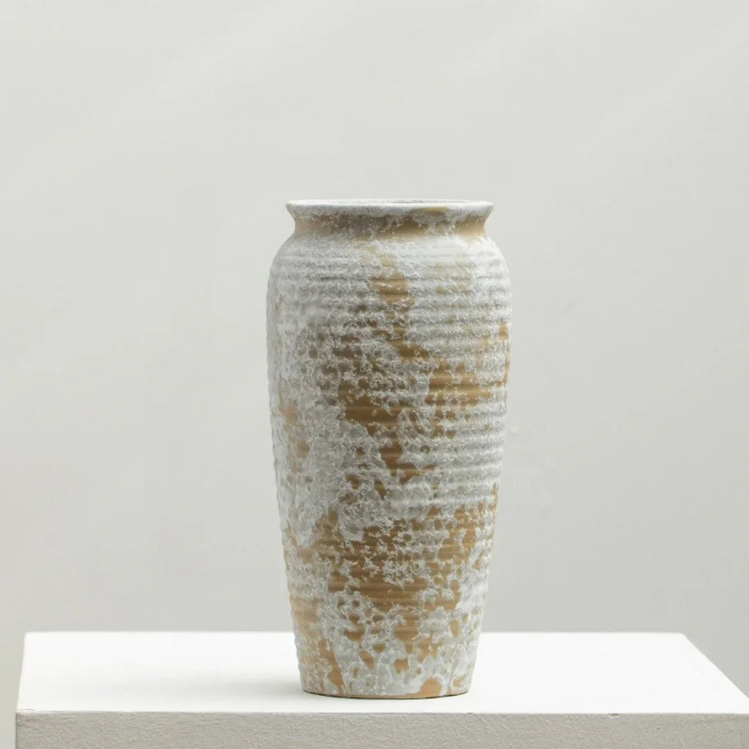 Textured ceramic vase with white and tan glaze on a minimalist white pedestal