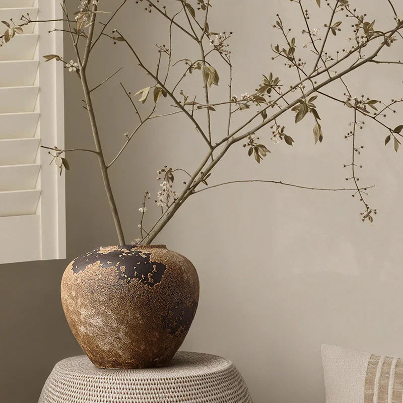 Rustic ceramic vase with dried branches and blossoms on a neutral table indoors