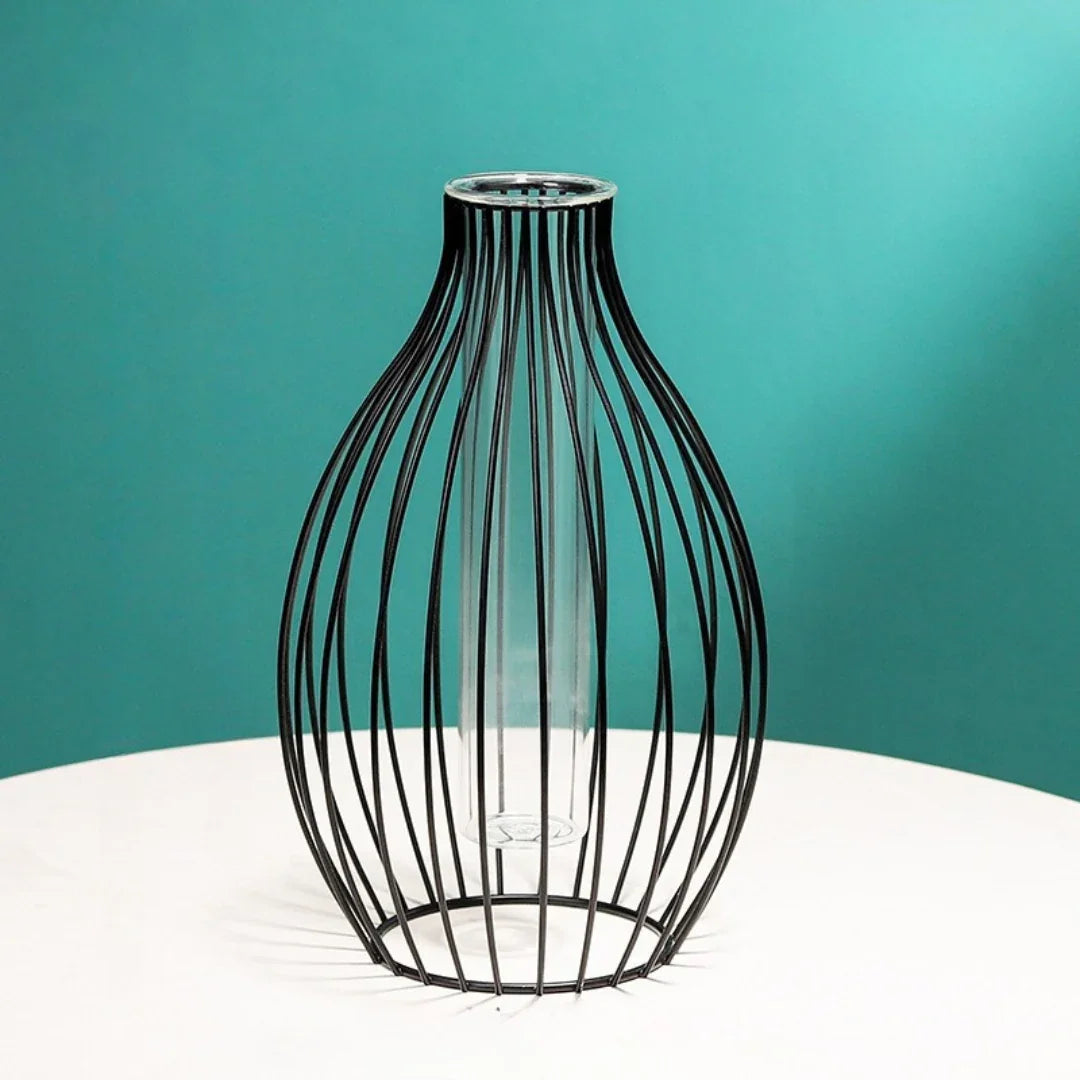 Modern decorative wire and glass vase on a white table with teal background